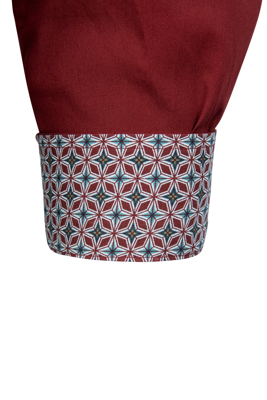 Close-up of a shirt cuff showing a solid burgundy upper section and a patterned lower cuff with a geometric star motif in burgundy, teal, and white.