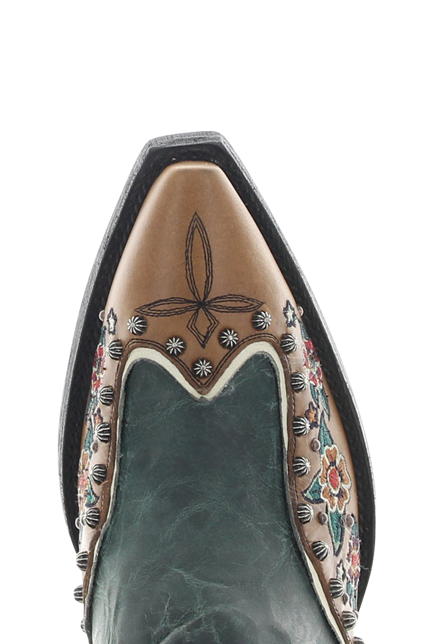 Close-up of a pointed-toe western boot showing the tan leather vamp with floral and geometric tooling, dark green leather sides, and silver conchos