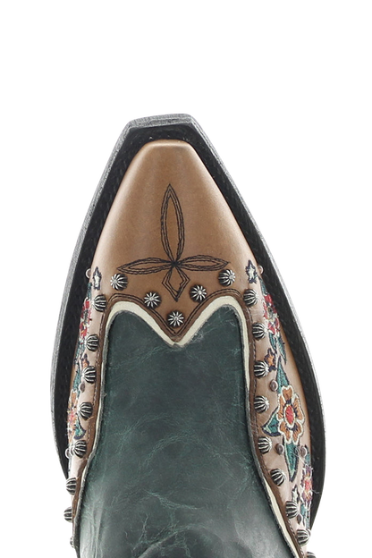 Close-up of a pointed-toe western boot showing the tan leather vamp with floral and geometric tooling, dark green leather sides, and silver conchos