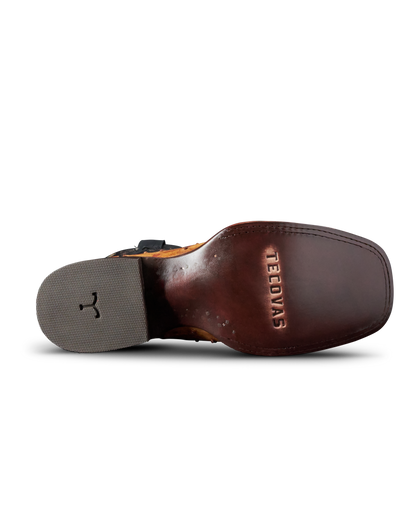 A close-up bottom view of a brown leather boot sole, showing the embossed brand name 'TEEDYAS' on the heel bed and a gray outsole with a black logo.